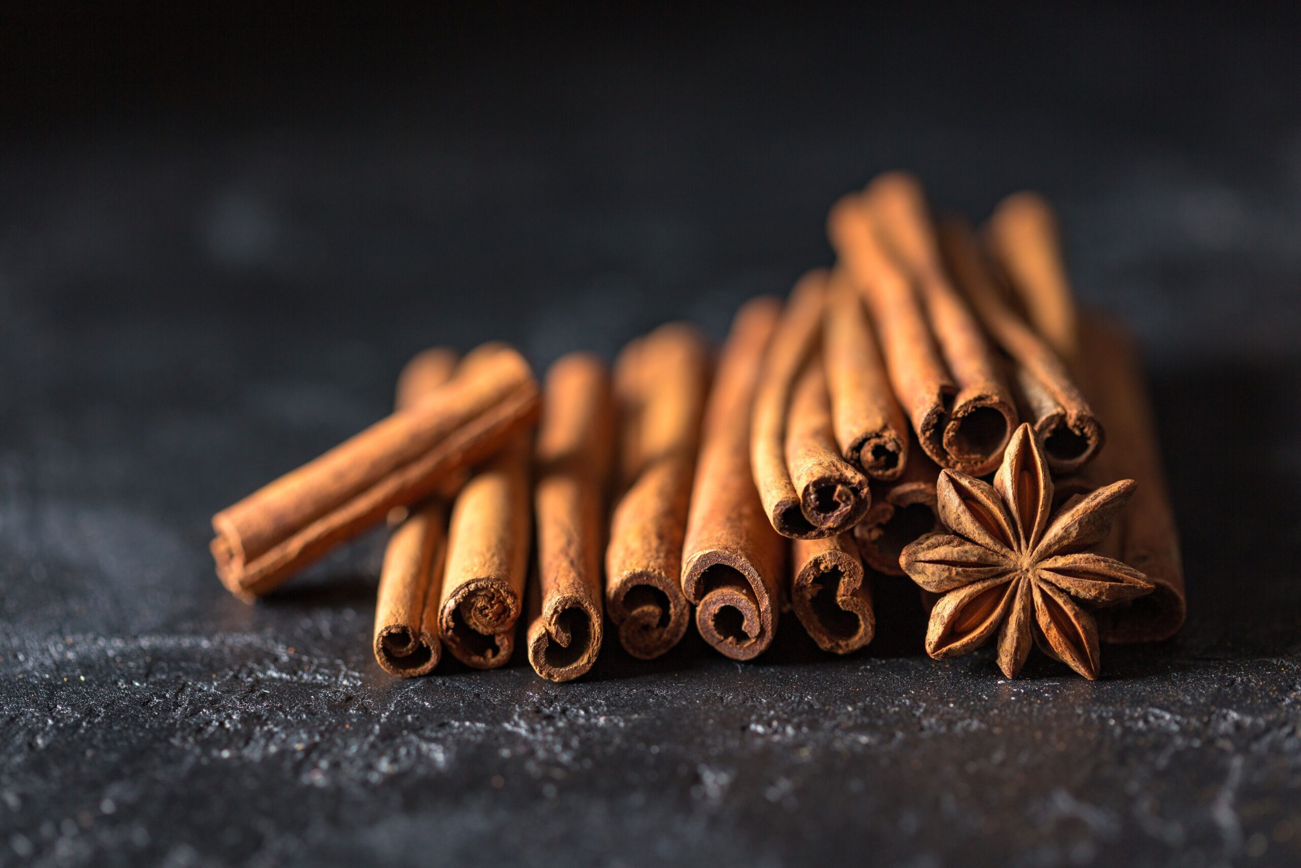 Indian spices Close-up of cinnamon sticks and star anise on a dark, textured surface, evoking warm, aromatic flavors.