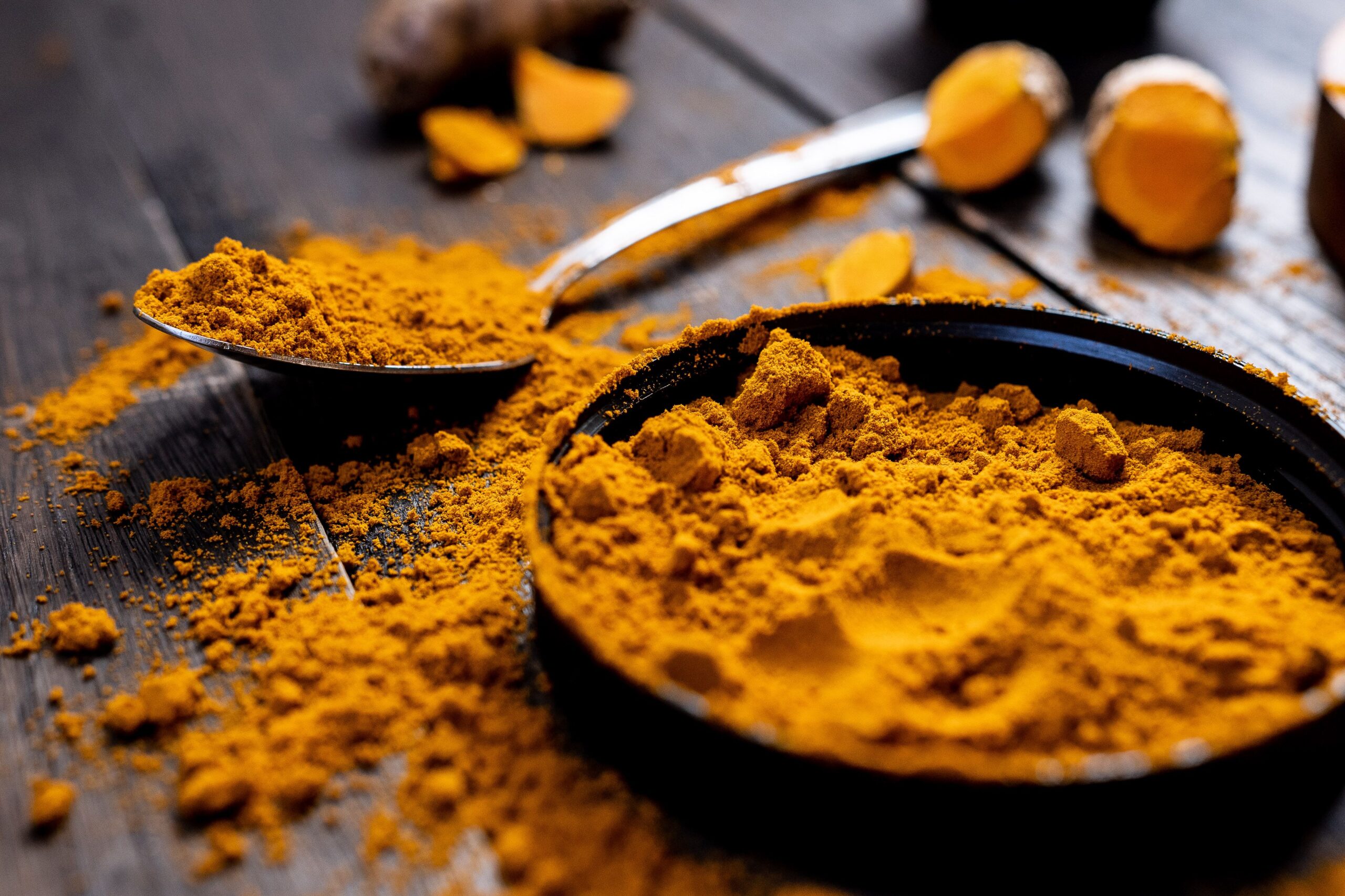Indian spices Close-up of vibrant turmeric powder with root on rustic wooden table, emphasizing texture and color.
