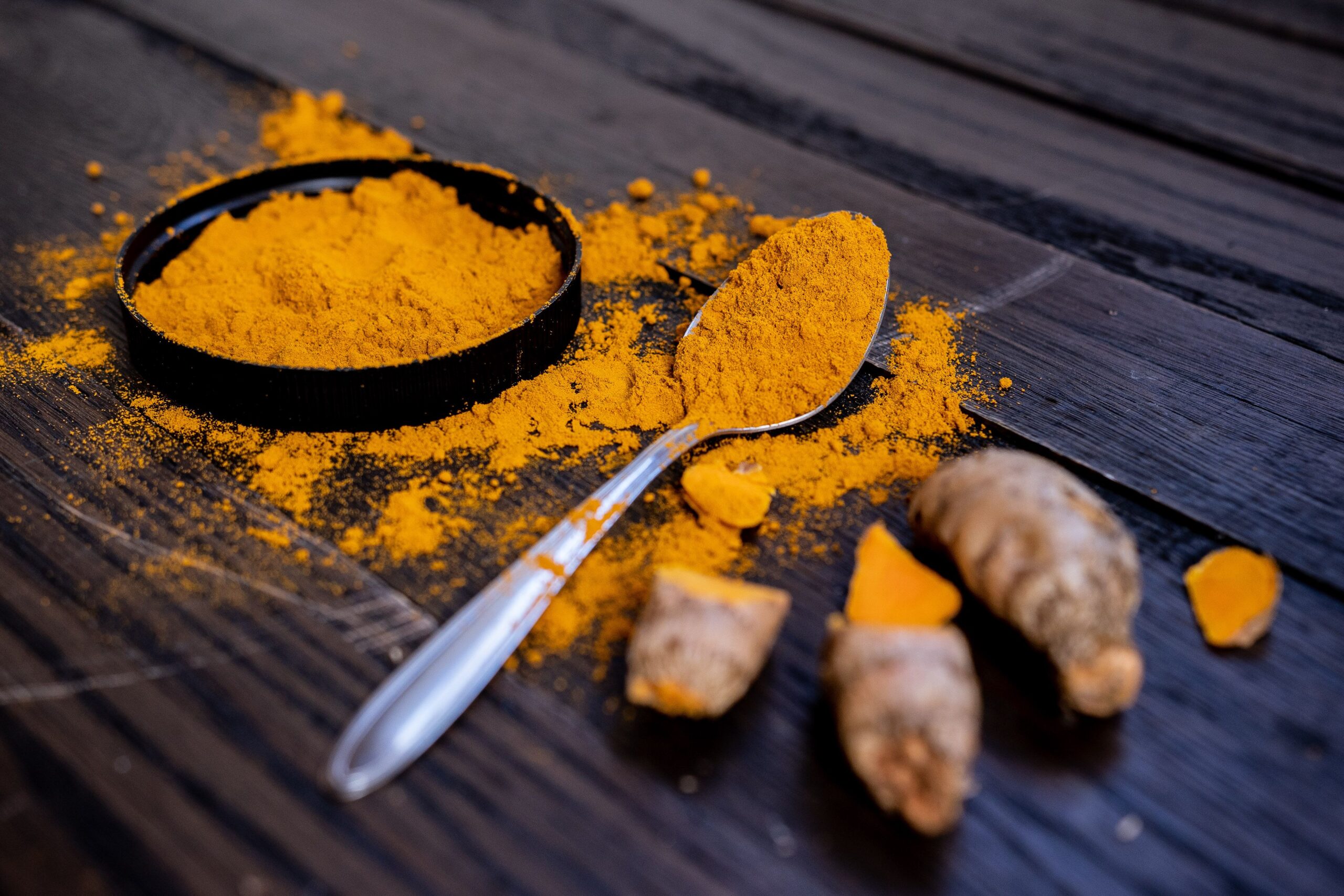 Indian spices Vibrant turmeric powder and root on a dark wooden surface, emphasizing natural spices.