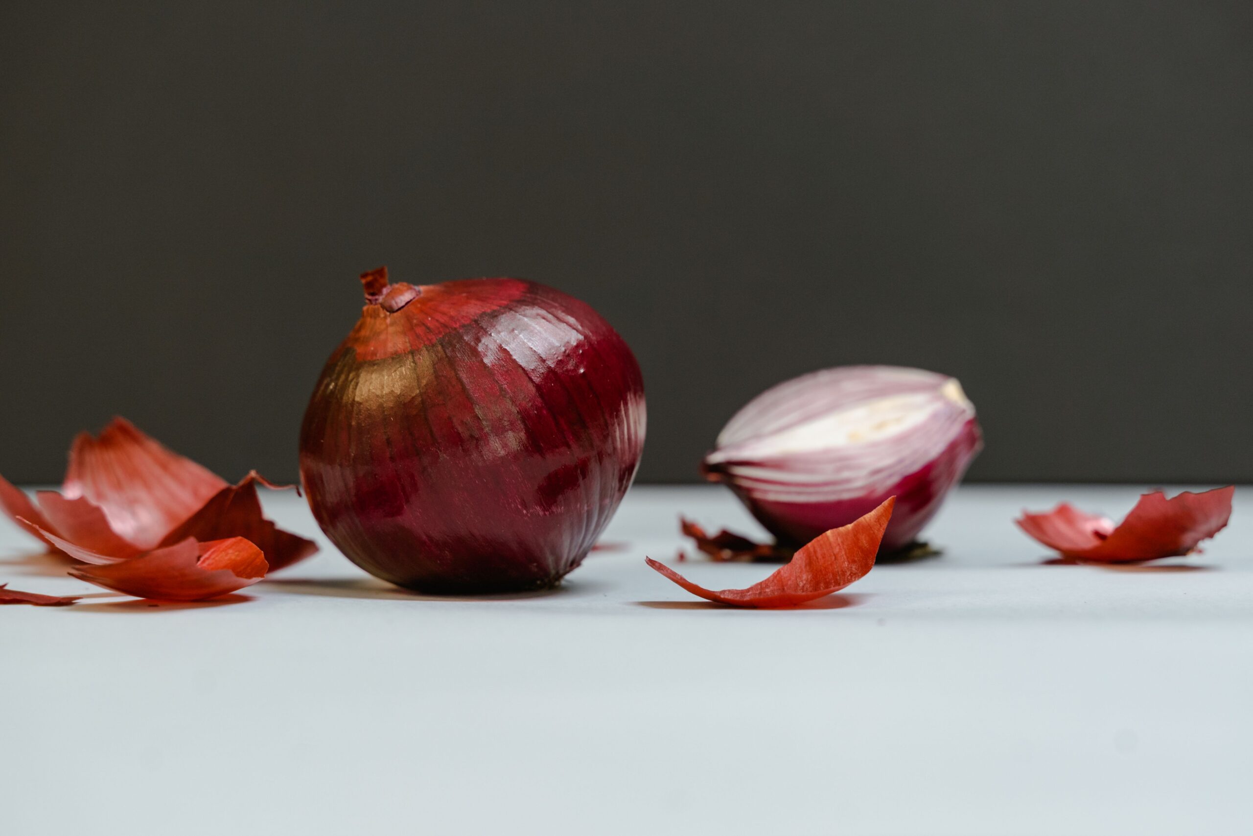 Indian spices Close-up of whole and sliced red onions with peeled skins on white surface.